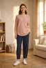 A woman modeling a light pink ribbed knit sweater and navy blue cropped trousers, standing against a plain light gray studio background.