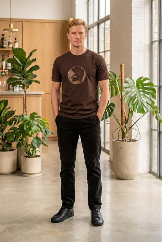 A dark brown short-sleeve crewneck t-shirt featuring a circular graphic on the chest with a Spartan helmet design in a beige and black houndstooth pattern, shown against a plain white background.