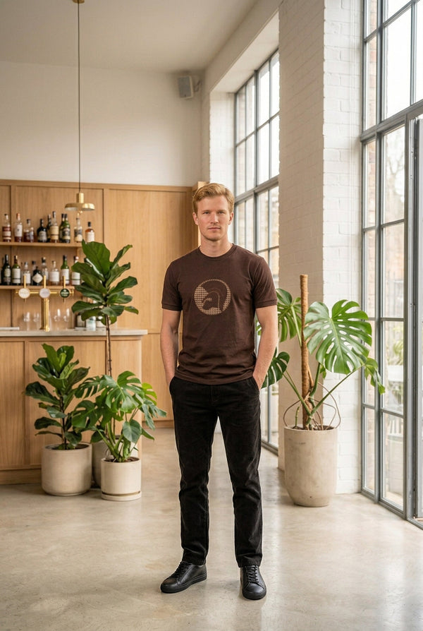 A dark brown short-sleeve crewneck t-shirt featuring a circular graphic on the chest with a Spartan helmet design in a beige and black houndstooth pattern, shown against a plain white background.